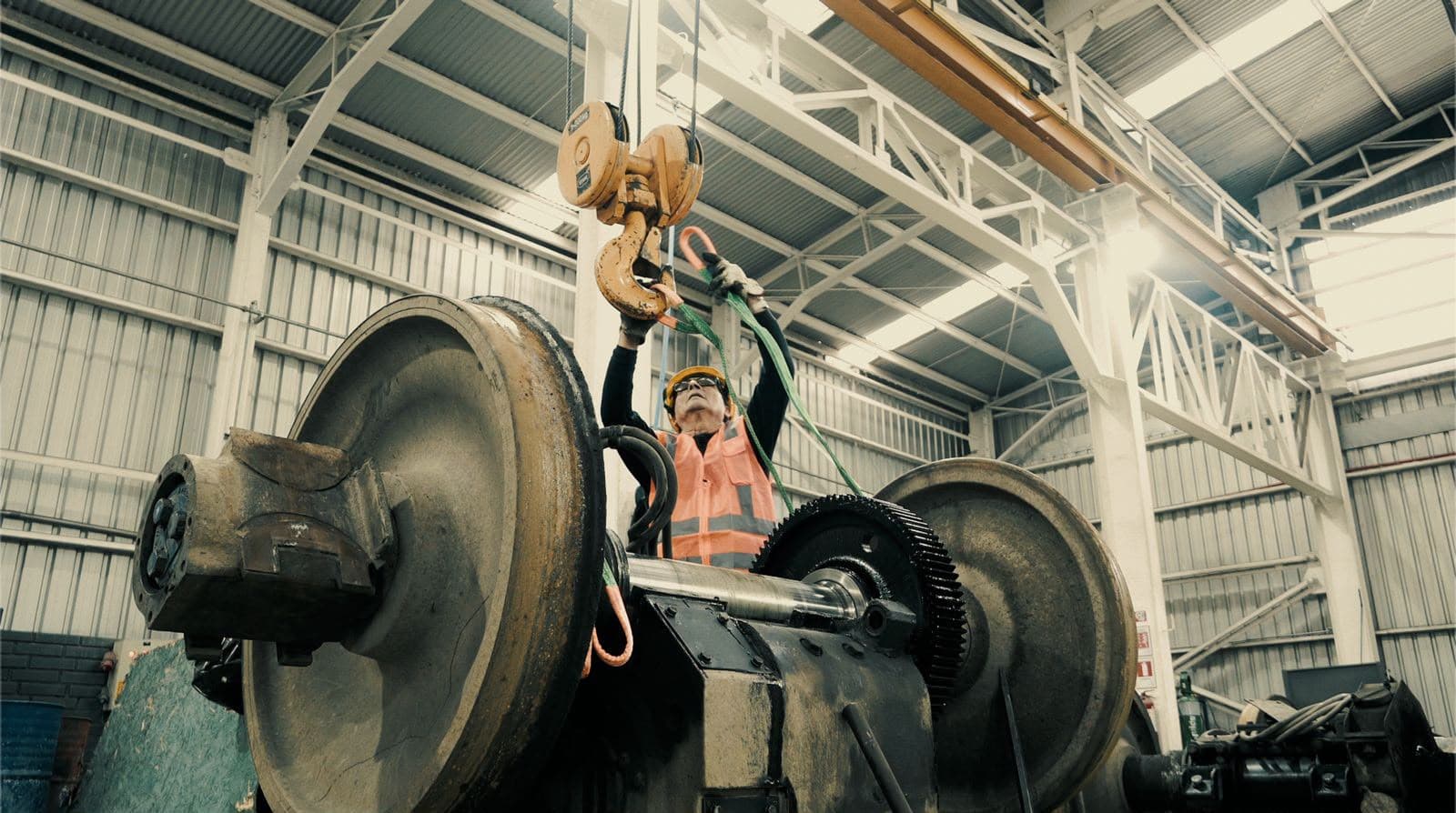 Técnico enganchando la eslinga al gancho del puente grúa sobre un par montado de locomotora con su corona dentada