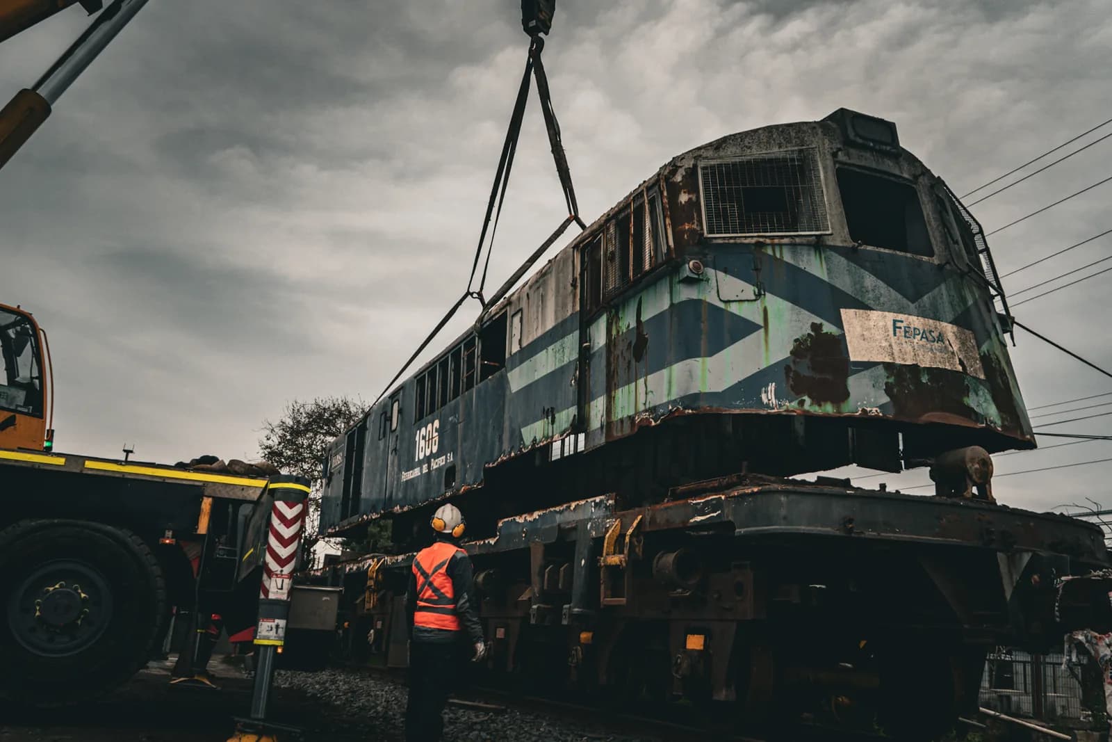 Locomotora suspendida por eslingas junto a la pluma de la grúa durante la maniobra de carga