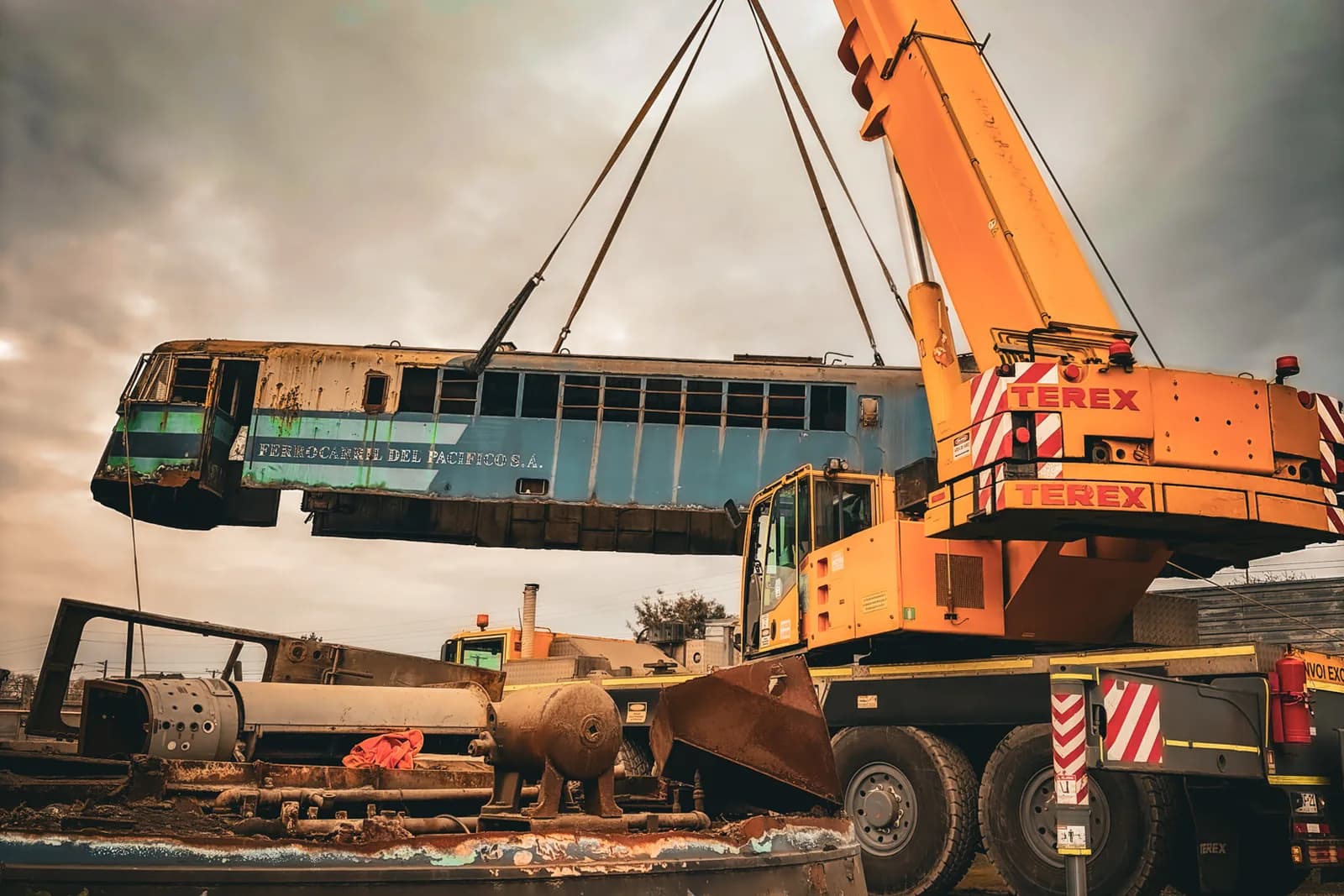 Grúa de gran tonelaje izando el cuerpo de la locomotora 1606 sobre terreno abierto, con cielo nublado al atardecer