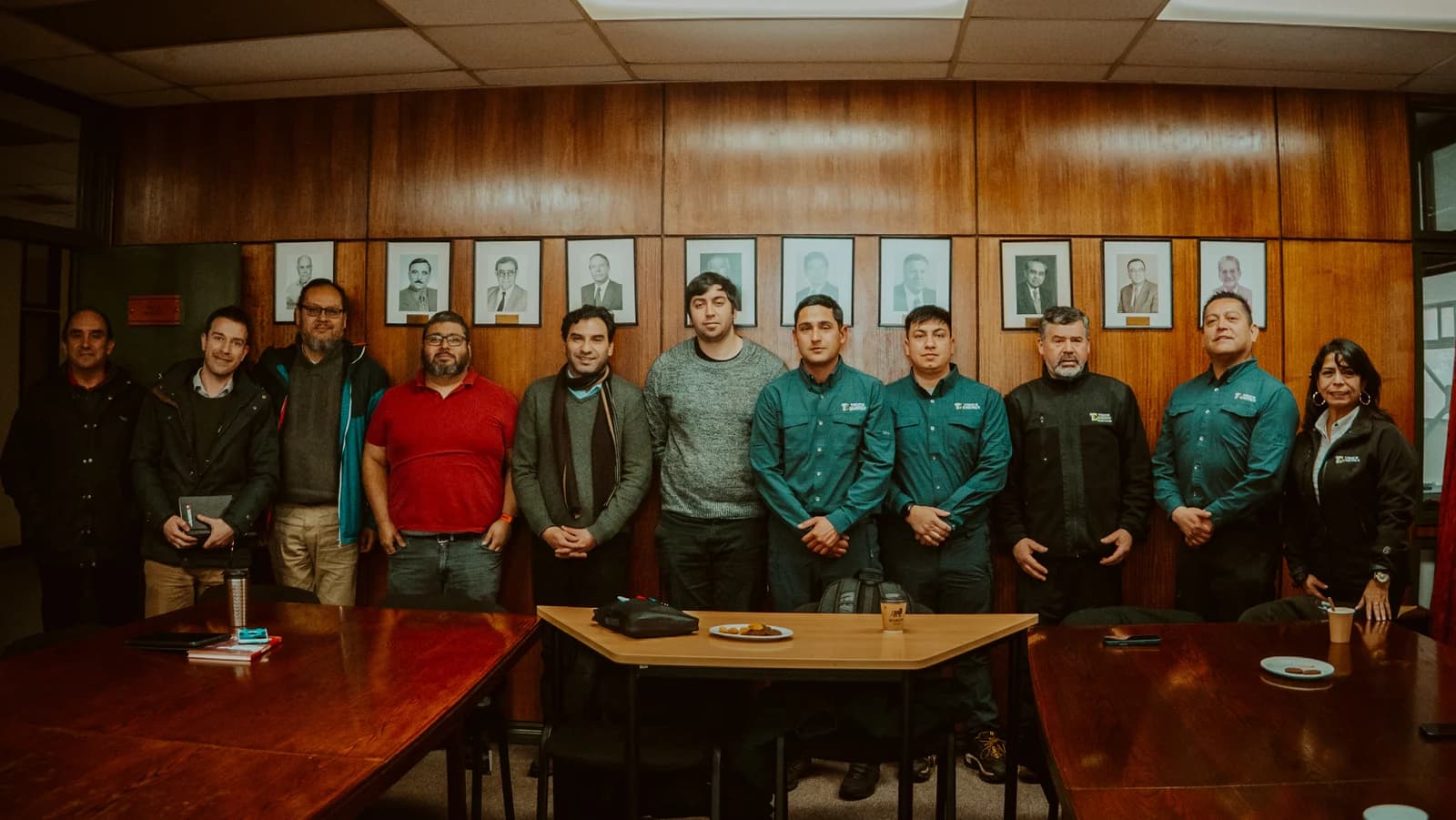 Los dos equipos posando juntos en la sala de consejo de la facultad, frente al muro de madera con los retratos enmarcados de los antiguos decanos