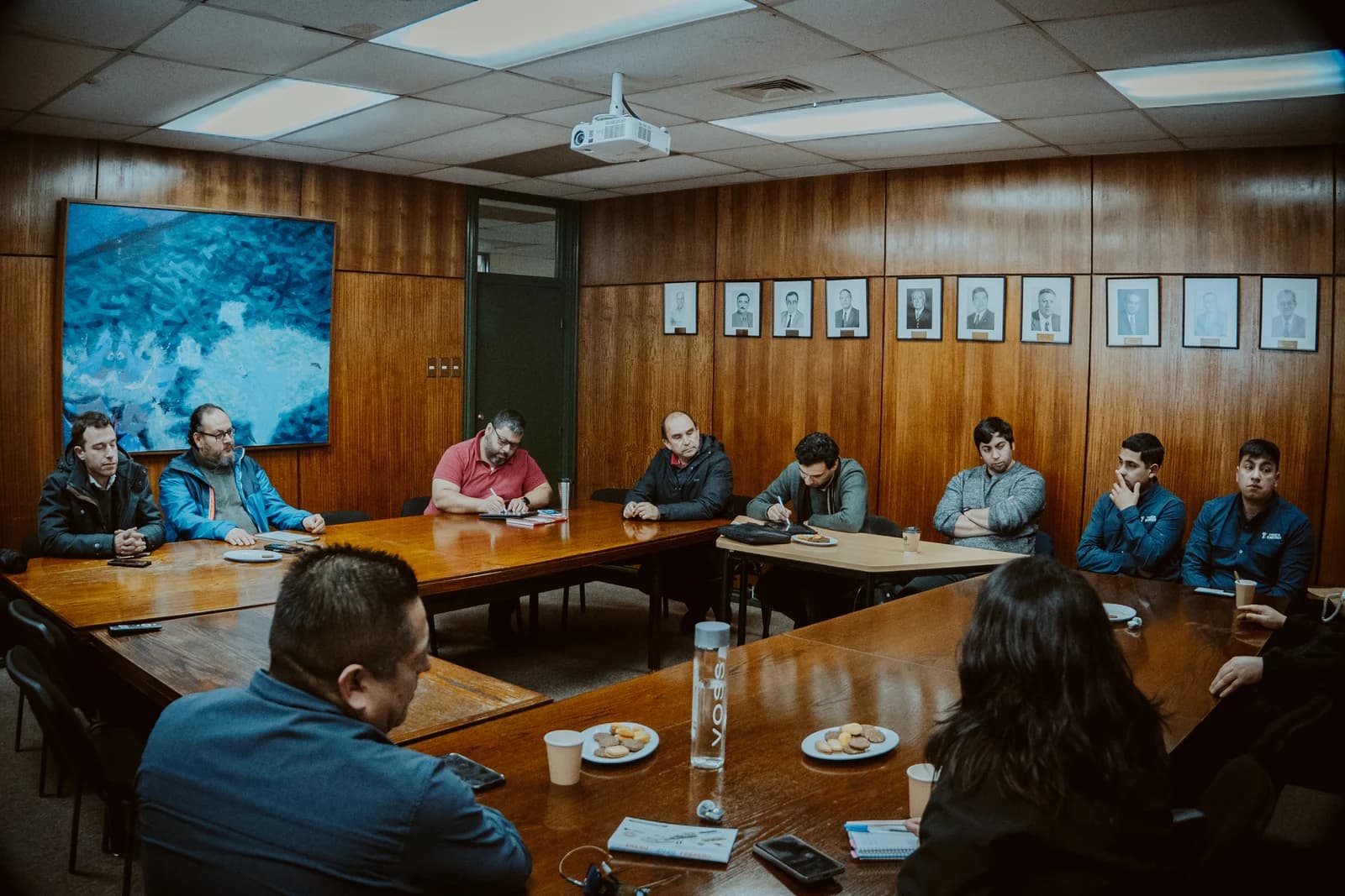 Vista general de la reunión: académicos y técnicos de Truck Energy sentados alrededor de la mesa en U de la sala de consejo