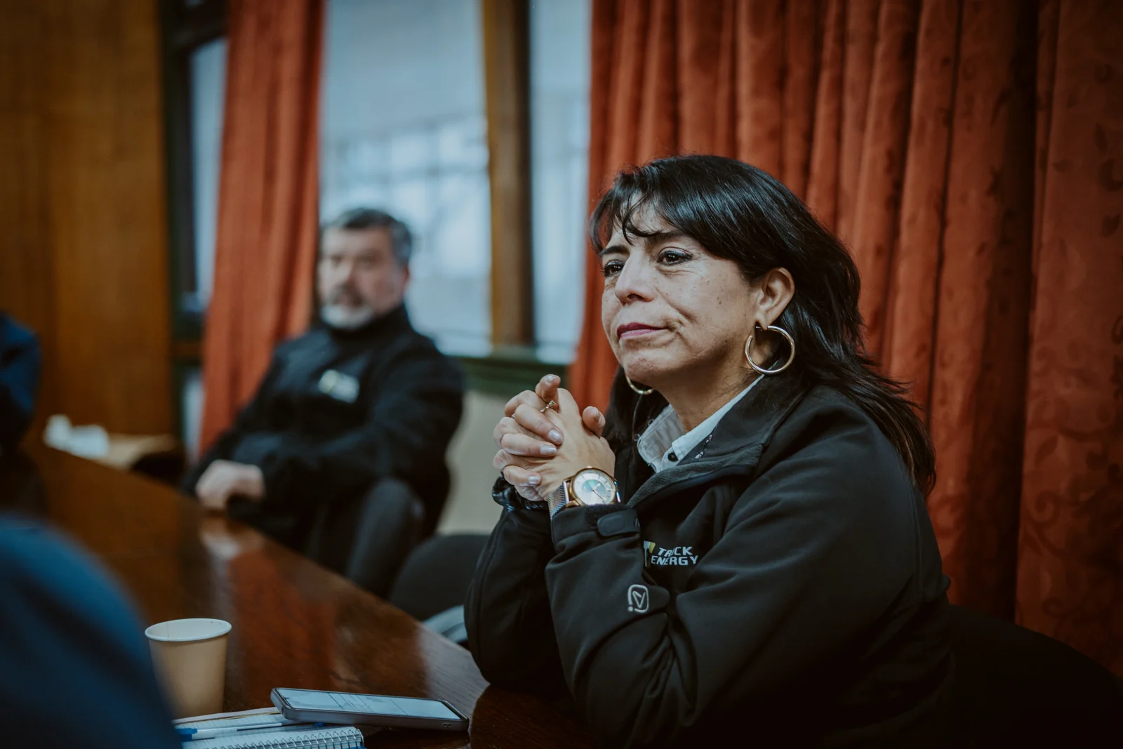 Una integrante del equipo de Truck Energy, con chaqueta institucional, escuchando con las manos entrelazadas sobre la mesa