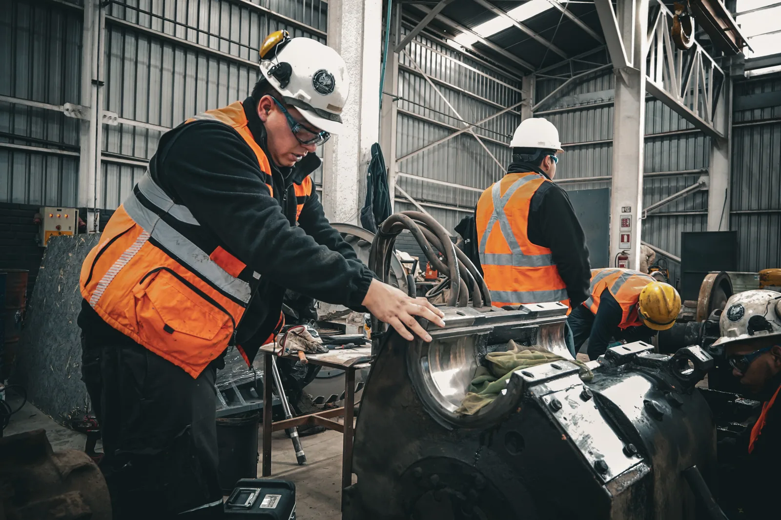 Technician recording measurements on a dismounted component, with a second technician at the back of the workshop