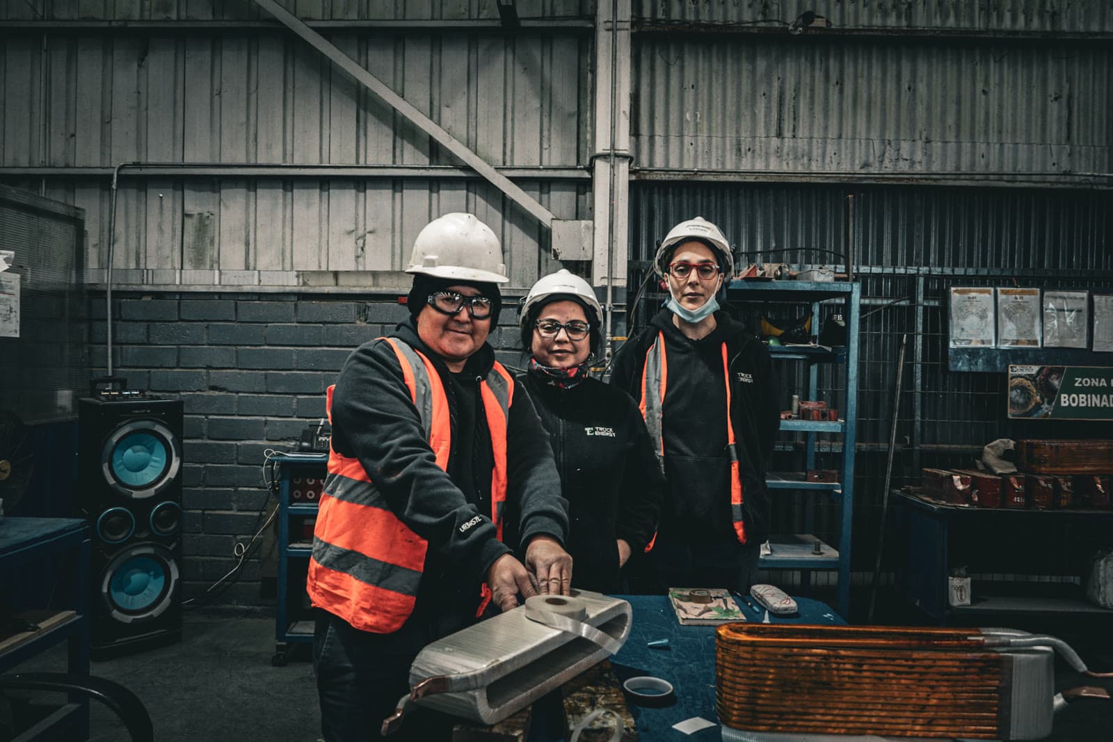 Tres integrantes del equipo de Truck Energy, con casco y chaleco reflectante, en el sector de bobinados del taller de Coronel, junto a una bobina de cobre sobre el banco de trabajo
