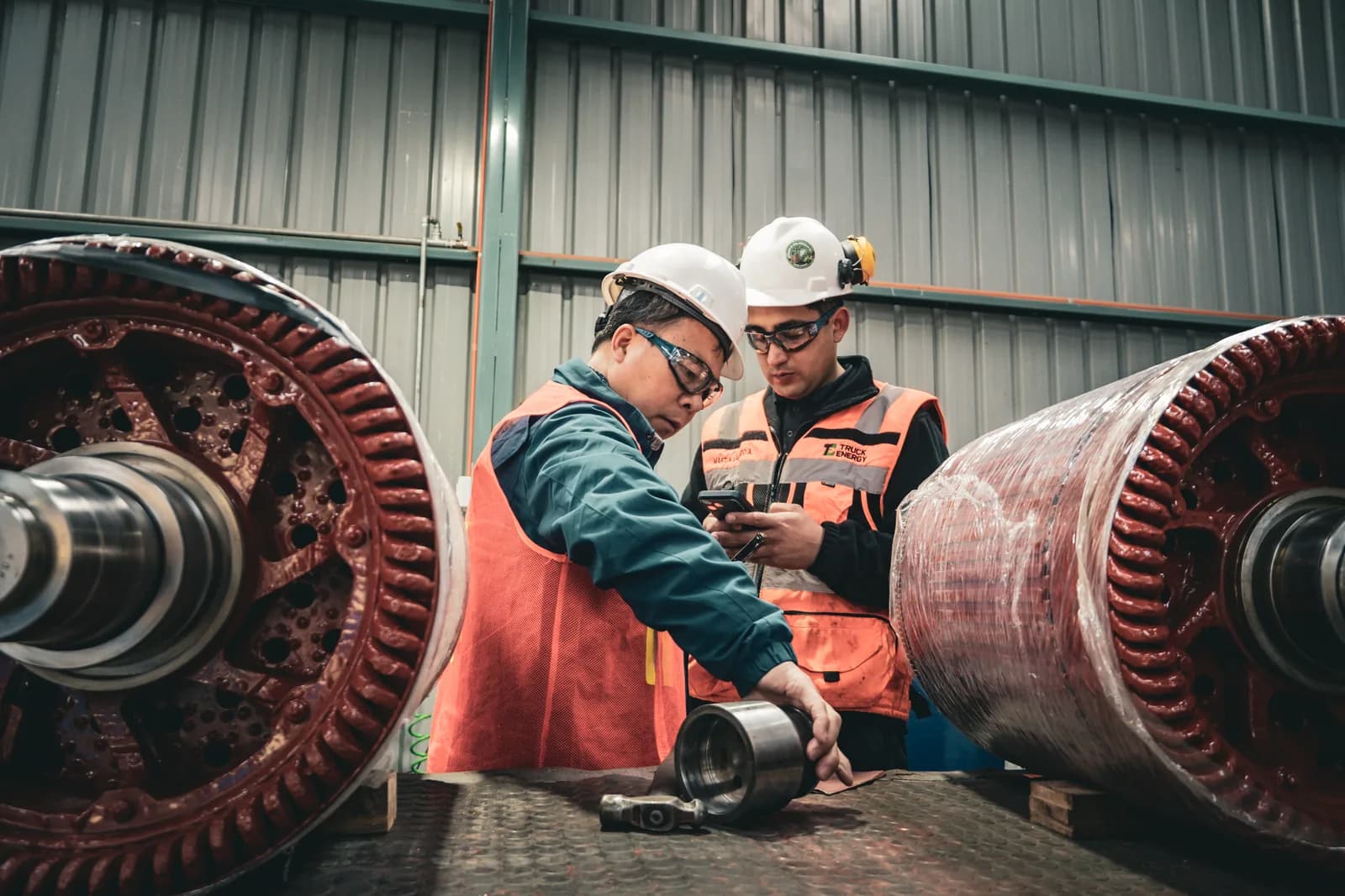 El ingeniero visitante y un técnico de Truck Energy inspeccionando el eje de un inducido de motor de tracción apoyado en el piso del taller